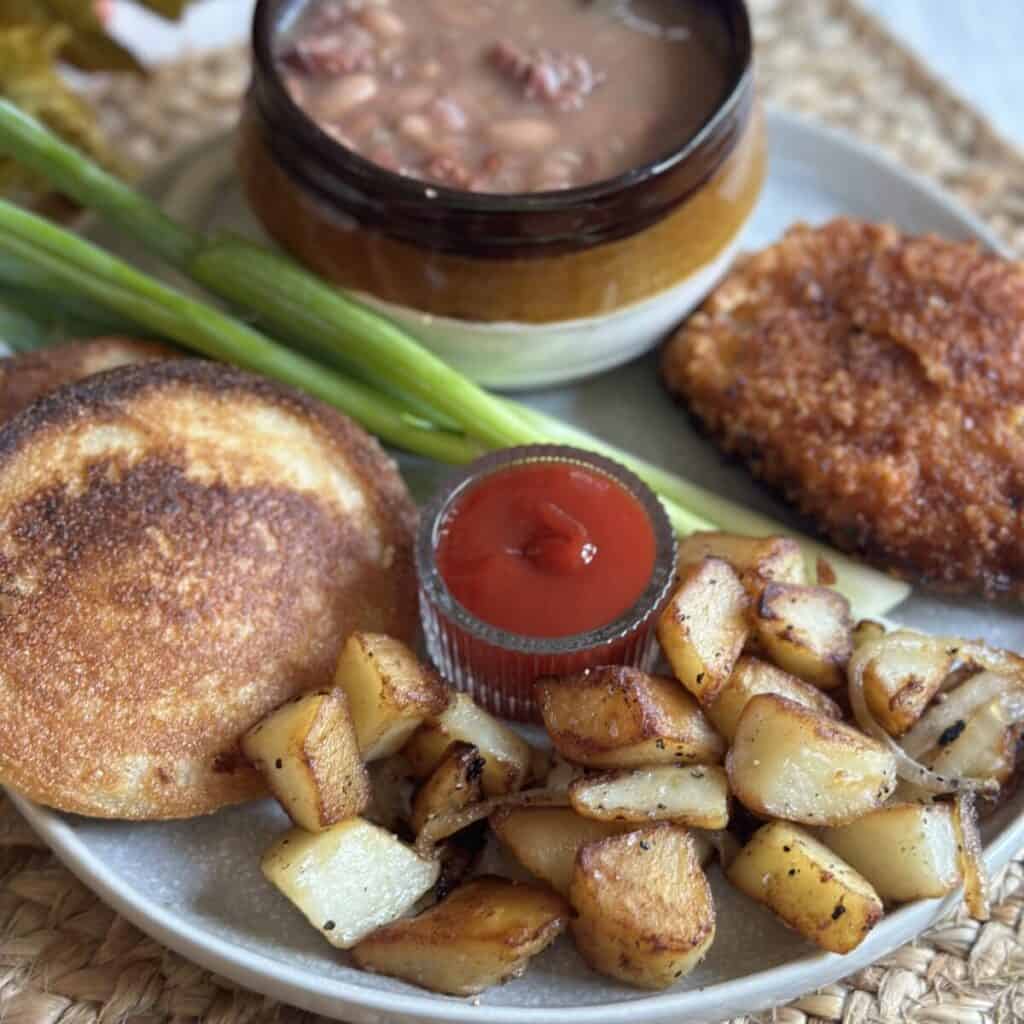 A plate with soup beans, hoecakes, a pork chop, and fried potatoes and onions.