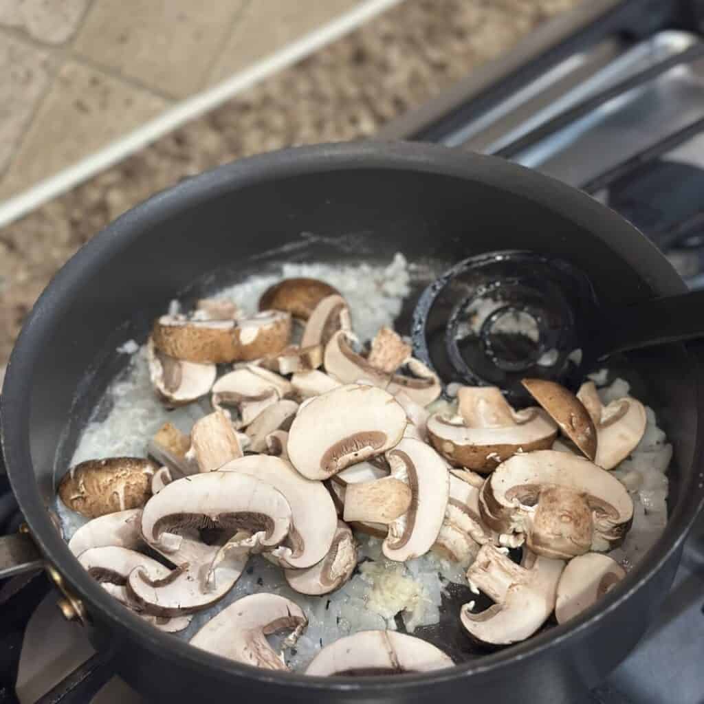 Sautéing mushrooms with onions and butter in a pan.