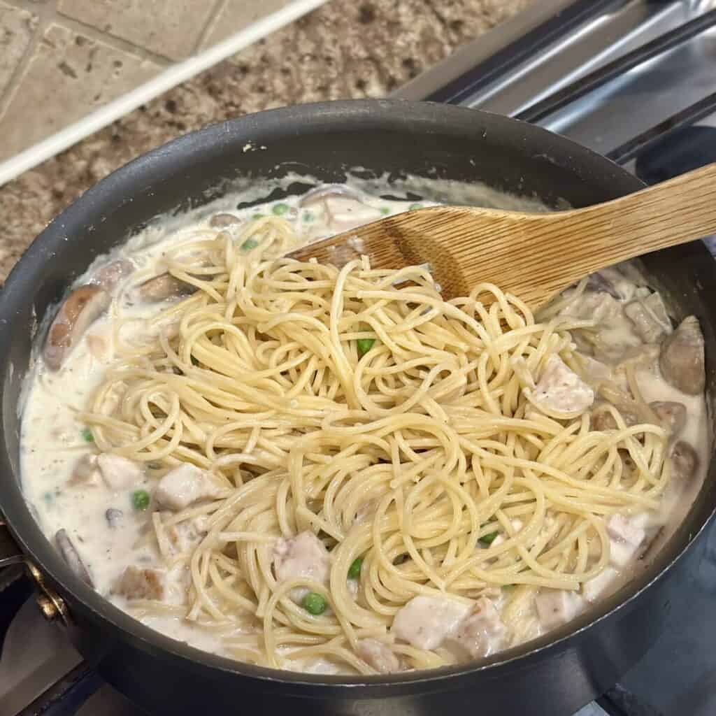 Adding spaghetti to the filling of turkey tetrazzini in a pan.