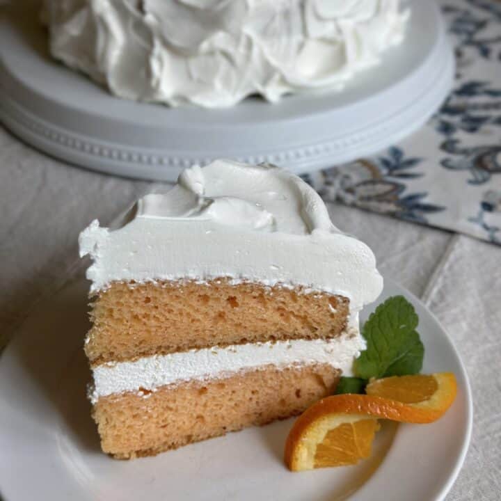A slice of dreamsicle cake on a saucer with an orange slice next to it.