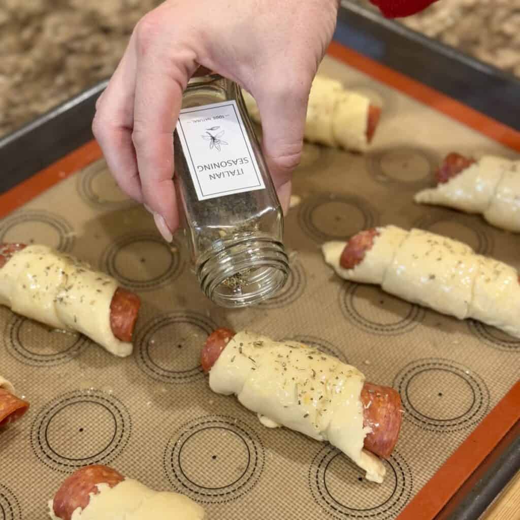 Sprinkling Italian seasoning on pizza crescent rolls