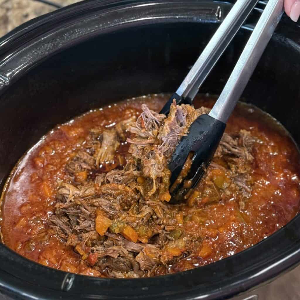 Adding beef short ribs to a crockpot of marinara sauce.