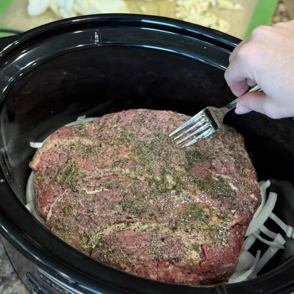 Roast beef in a crockpot with sliced onion.