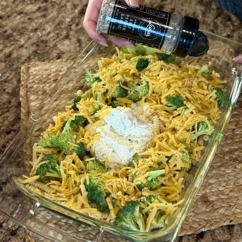 Adding seasonings to a dish of broccoli pasta bake.