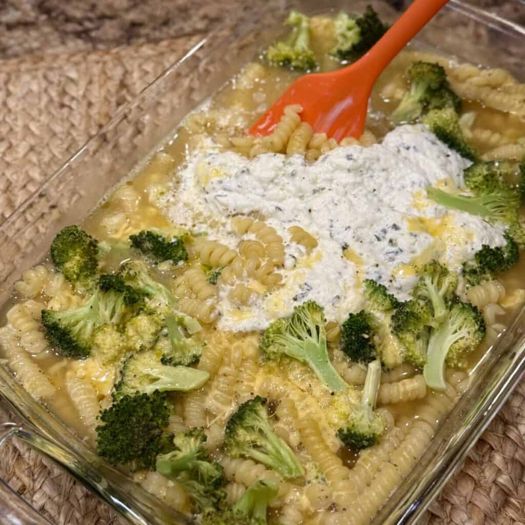 Mixing broccoli pasta bake in a dish.