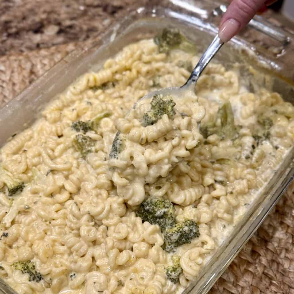 Stirring a broccoli pasta bake in a baking dish.