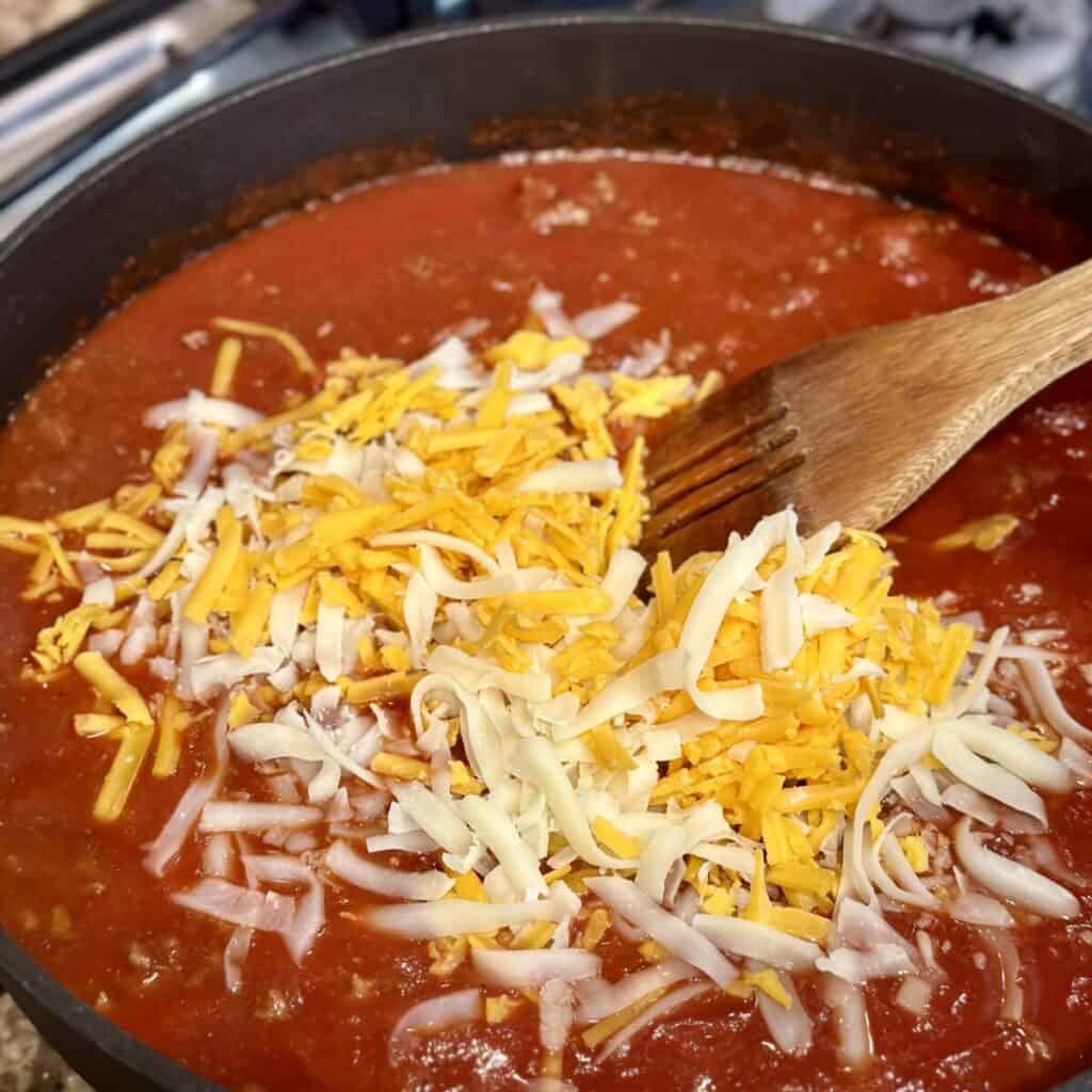 Adding cheese to tomato sauce in a pan.