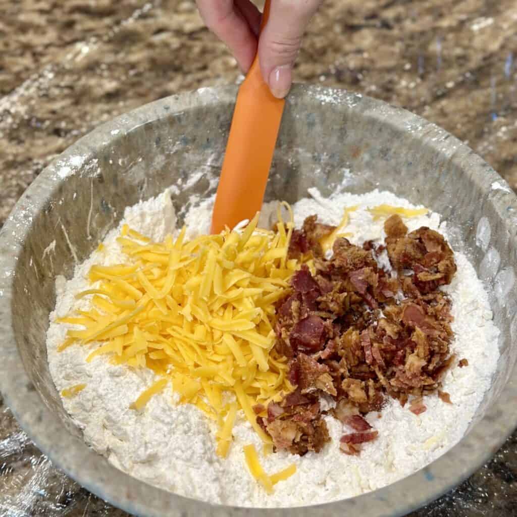 Mixing cheddar cheese and bacon in flour.