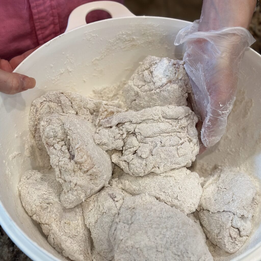 Coating chicken in flour in a bowl.