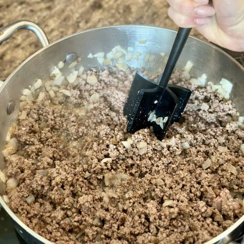 Breaking up ground beef in a skillet.