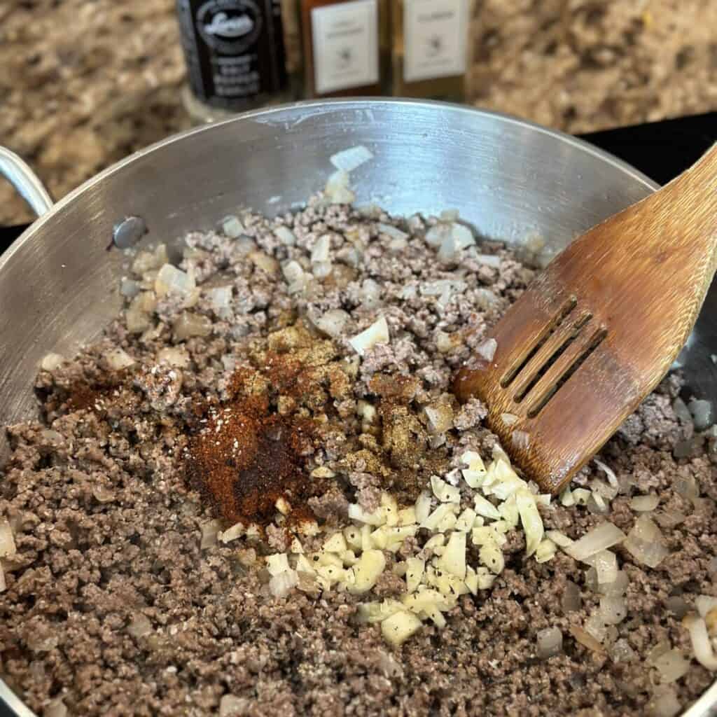 Sautéing seasonings with beef and onions in a skillet.