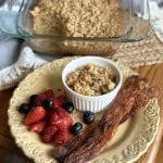 A plate with bacon, berries and bowl of oatmeal.