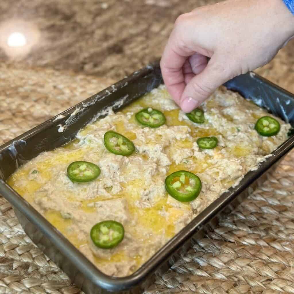 Adding jalapeños to the top of a loaf batter.