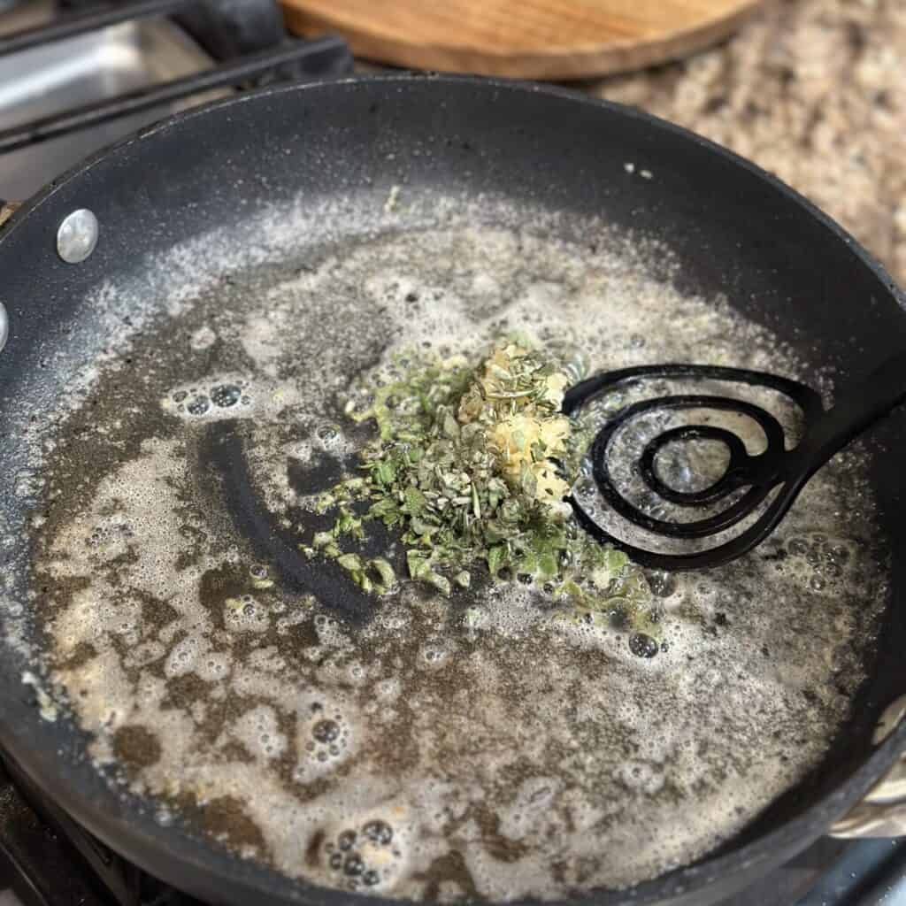 Mixing herbs and butter in a skillet.