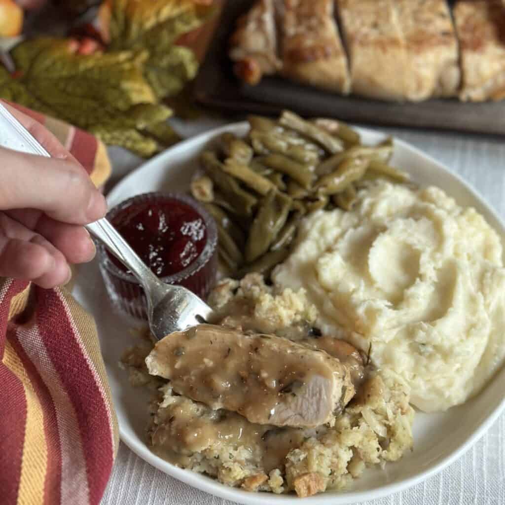 A plate with mashed potatoes, green beans, cranberry sauce, and turkey with gravy.