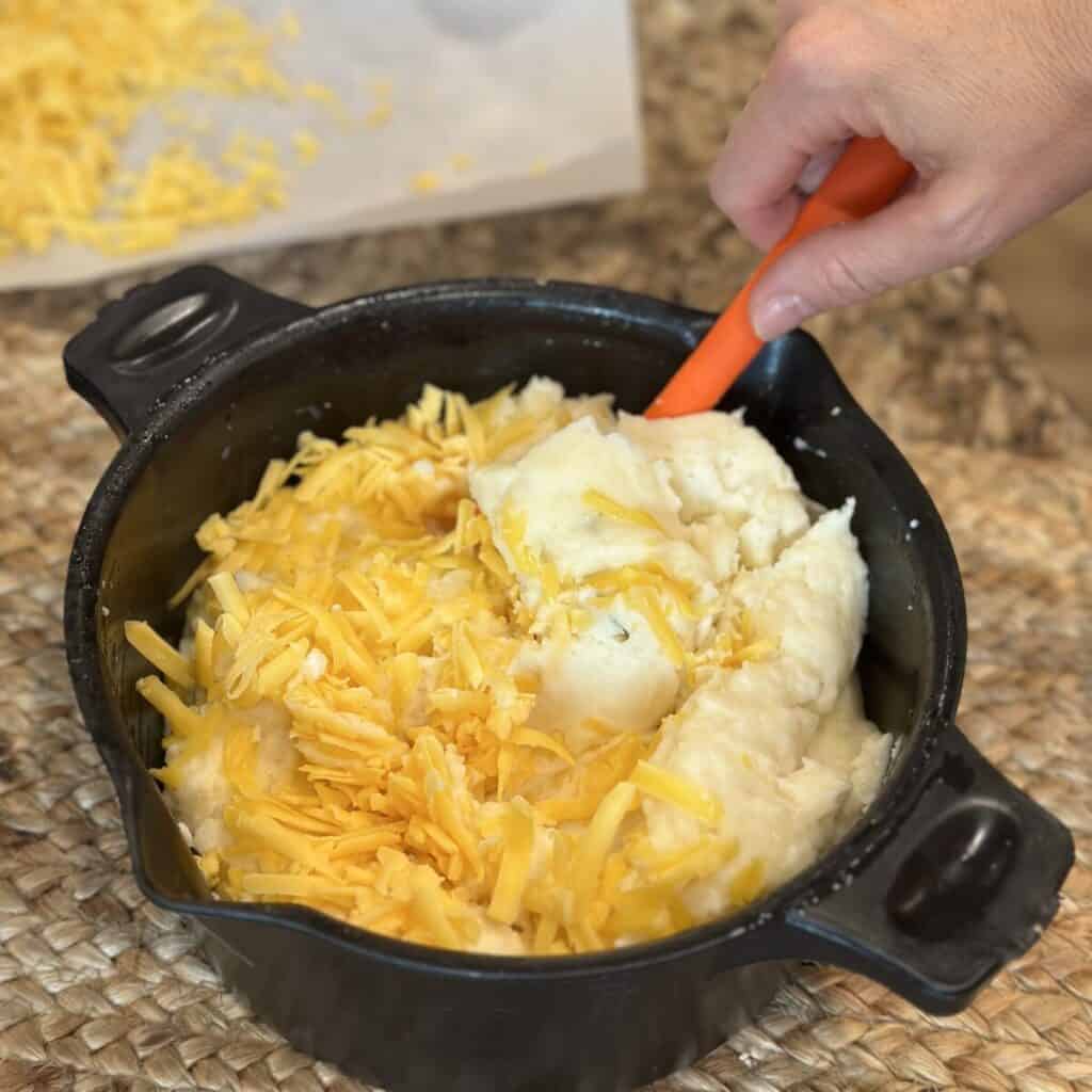 Mixing together cheese and mashed potatoes in a bowl.