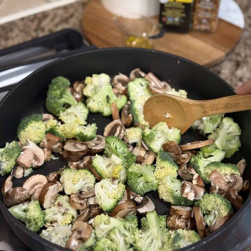 Stirring broccoli and mushrooms in a skillet.