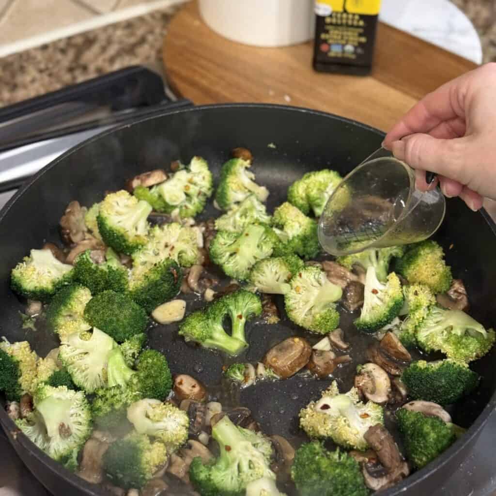 Adding water to mushrooms and broccoli in a skillet.