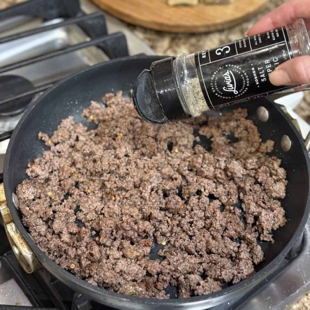 Seasoning ground beef in a pan.