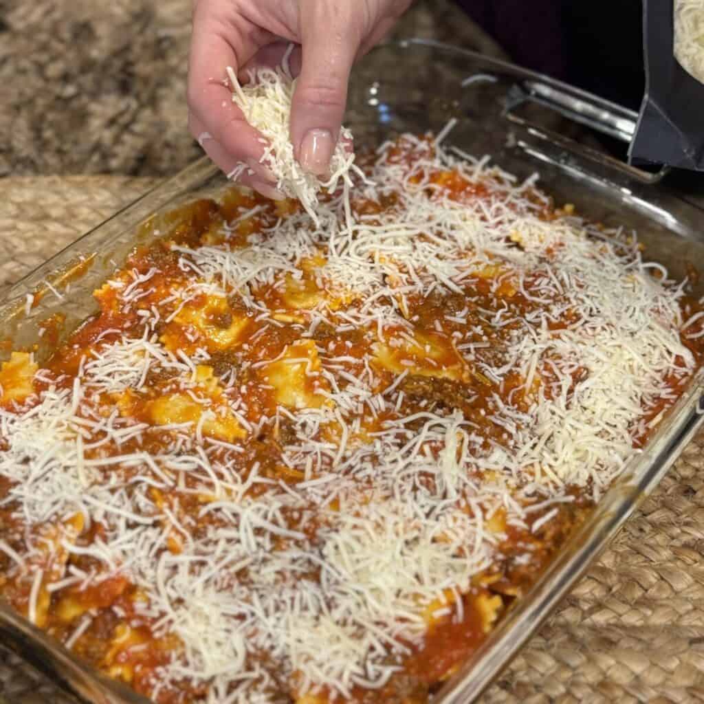 Adding cheese to the top of a baked ravioli recipe.