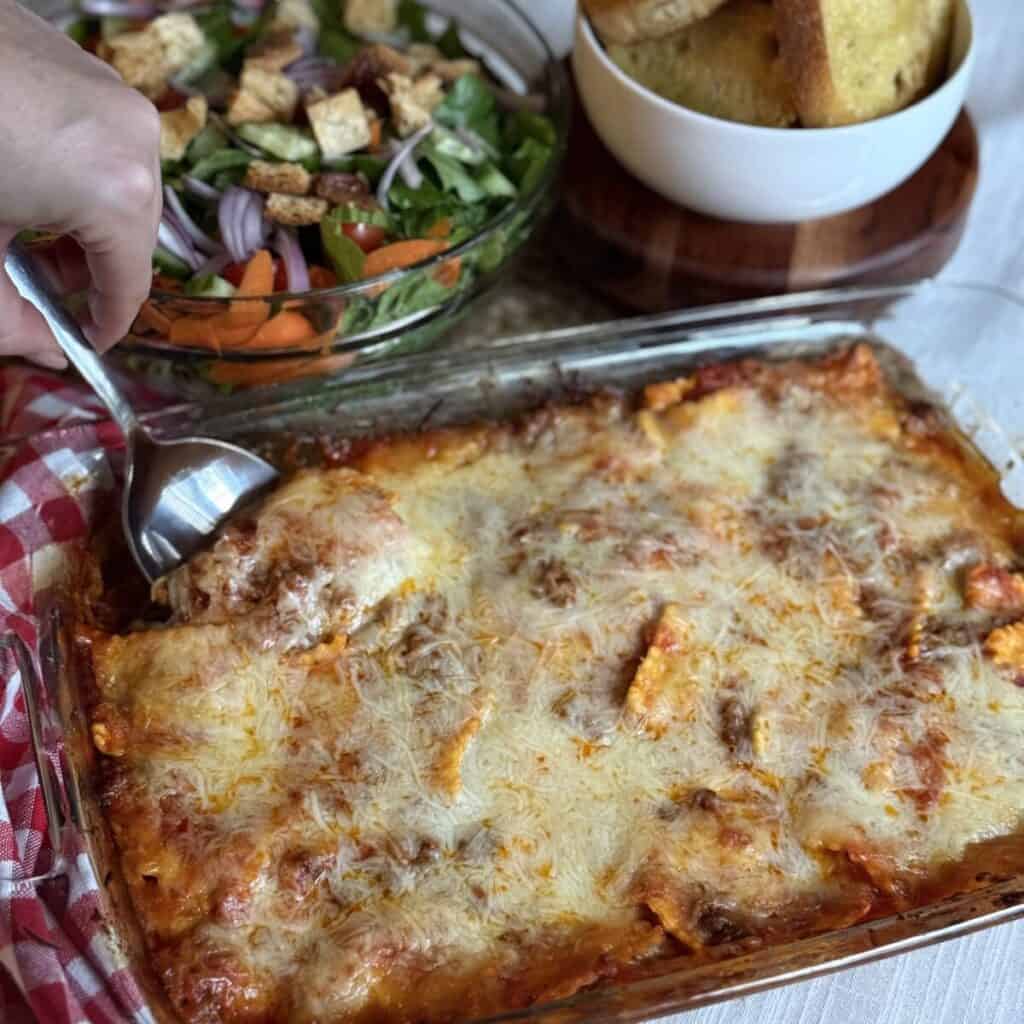 Scooping out baked ravioli from a dish.