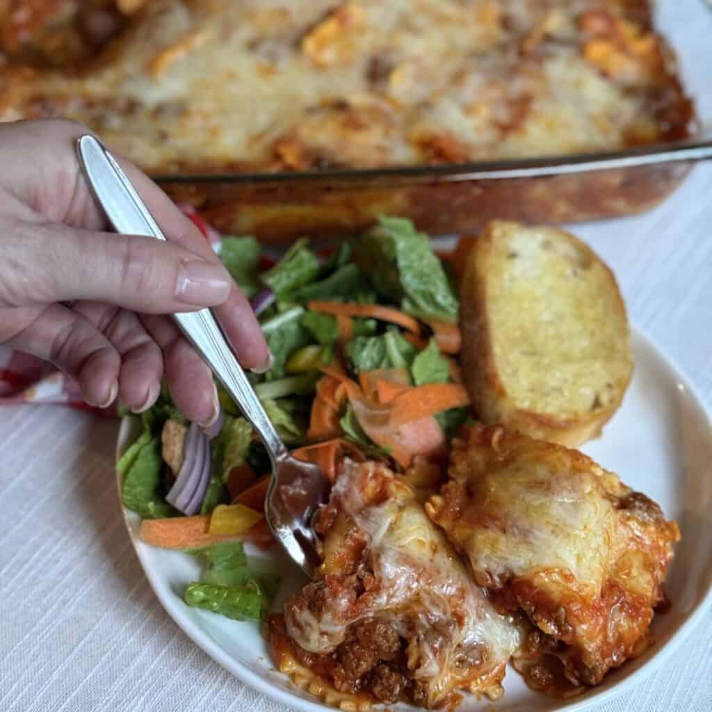 Baked ravioli recipe on a plate with a salad on the side.