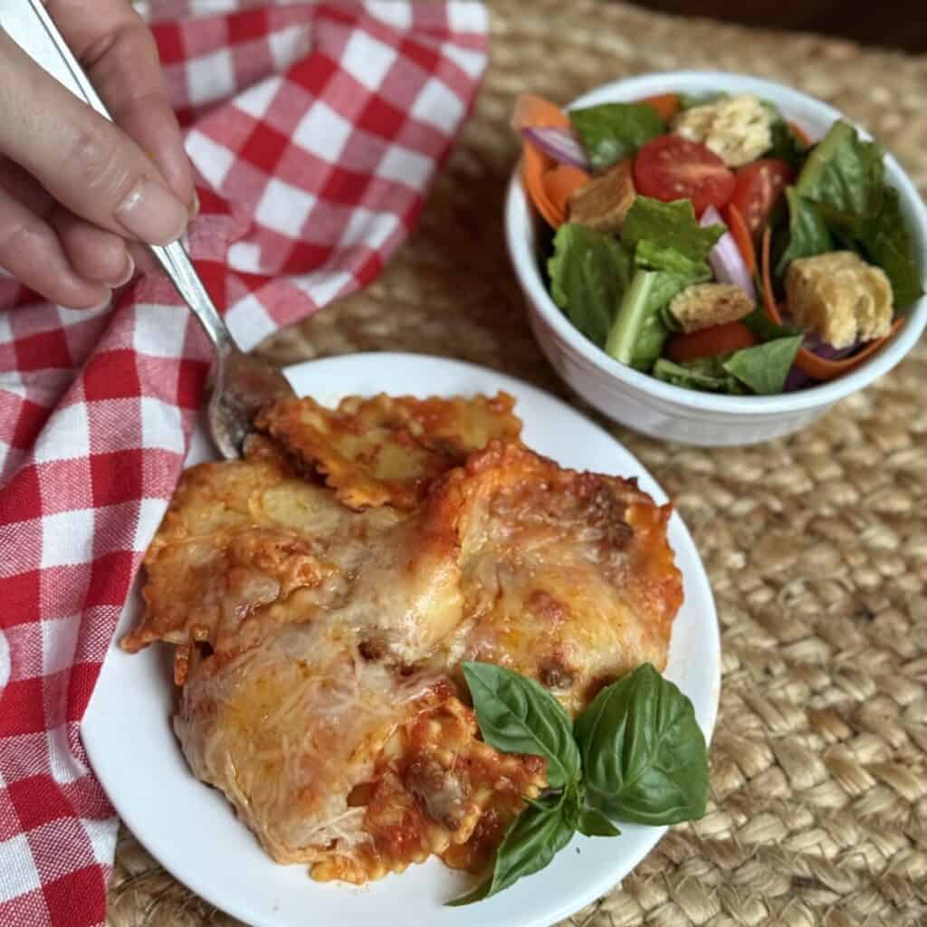 Baked ravioli recipe on a plate with a salad on the side.