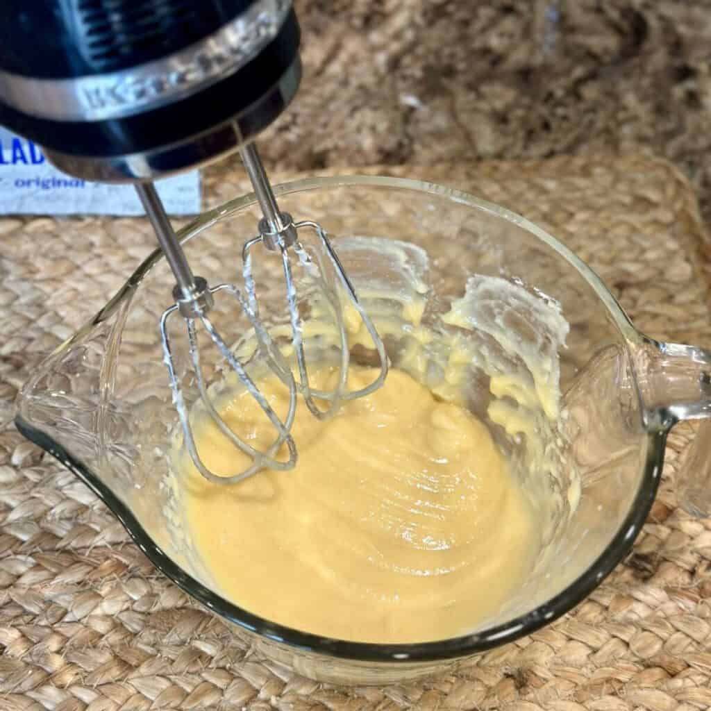 Beating together evaporated milk and cheesecake pudding mix in a bowl.