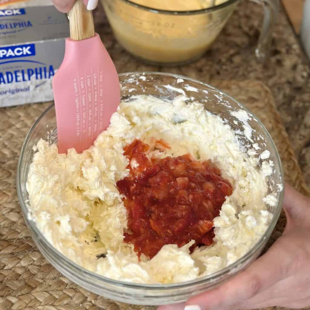 Folding chopped strawberries in a bowl of cream cheese.