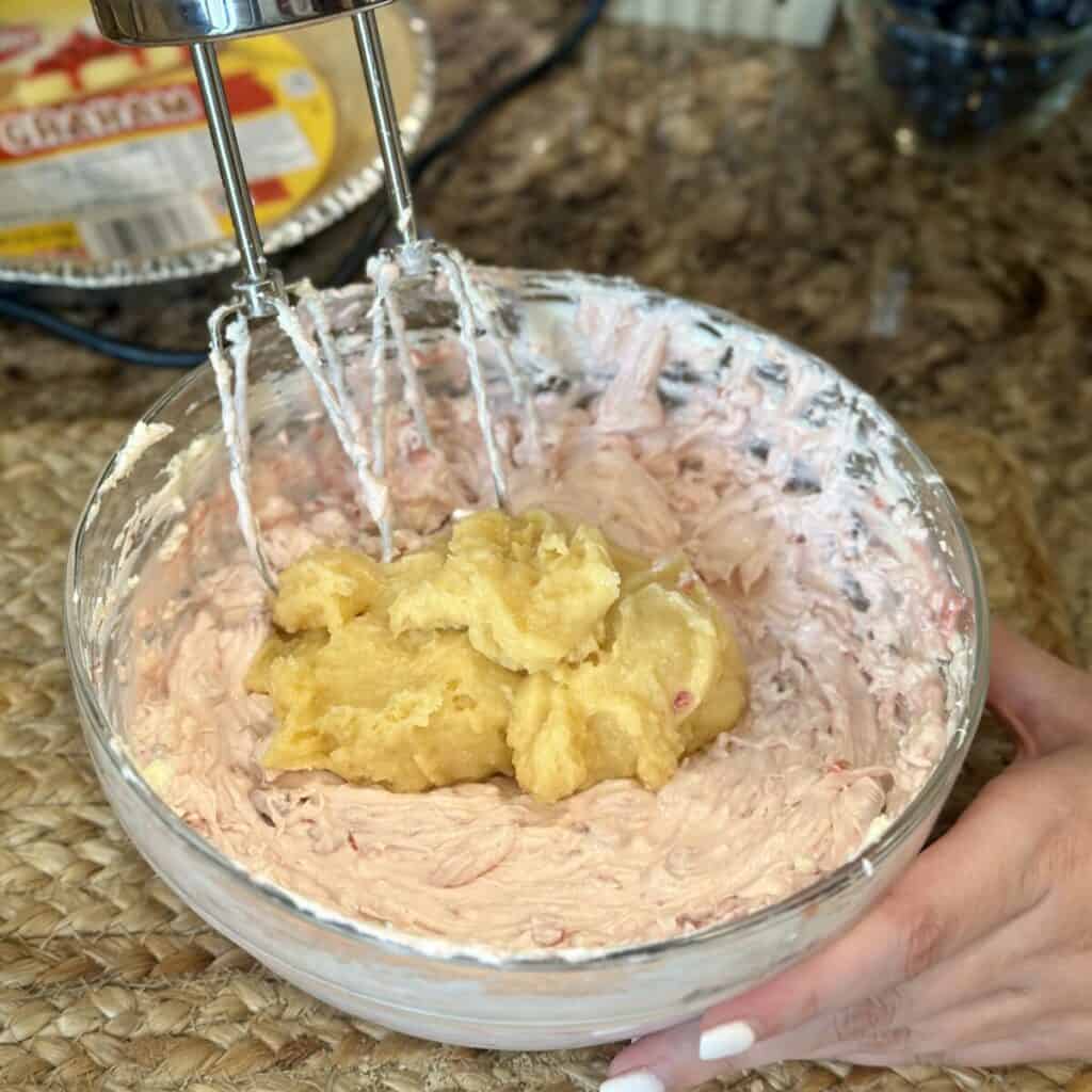 Folding a pudding mixture in a cream cheese mixture in a bowl for a pie.