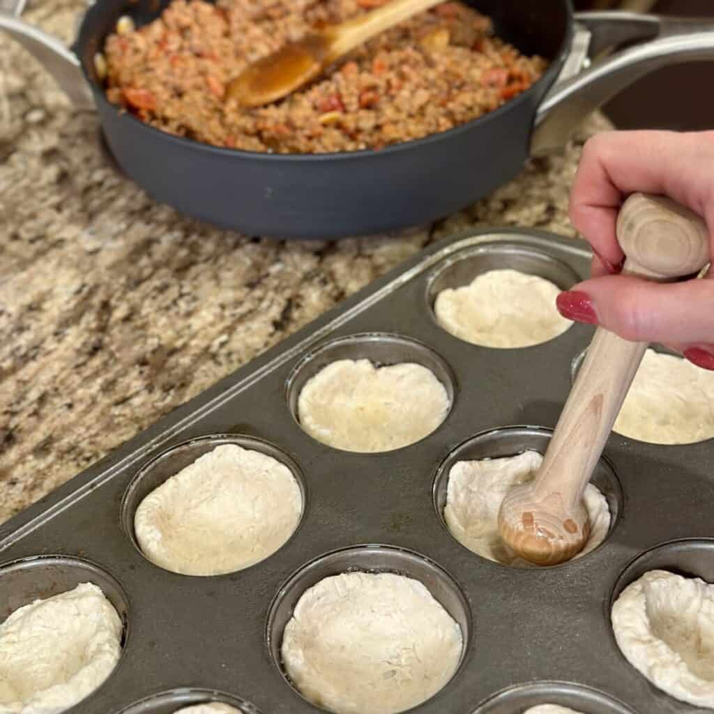 Tampering biscuit dough in a muffin pan.