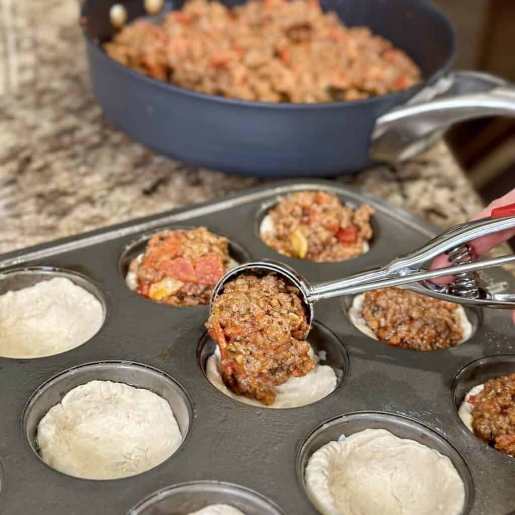 Adding pizza filling to biscuit dough in a muffin pan.