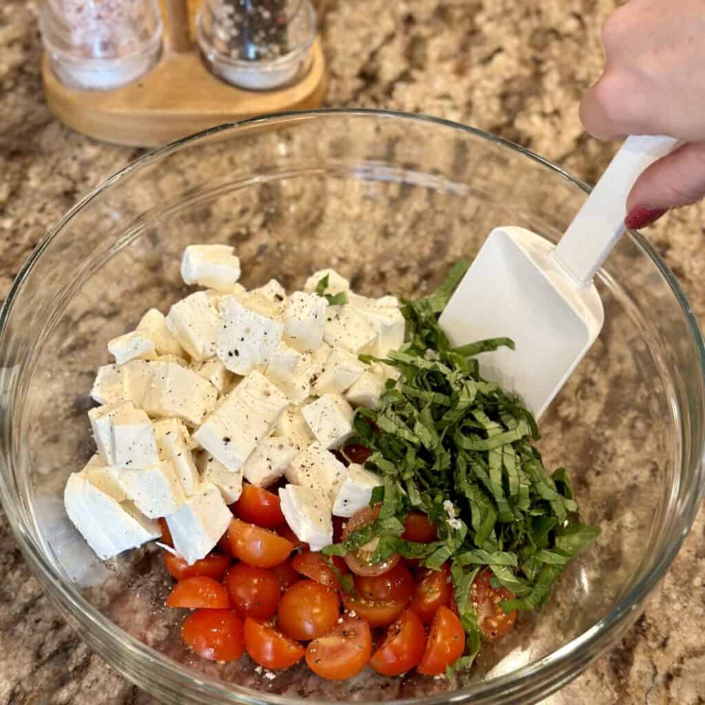 Mixing together caprese salad ingredients in a bowl.