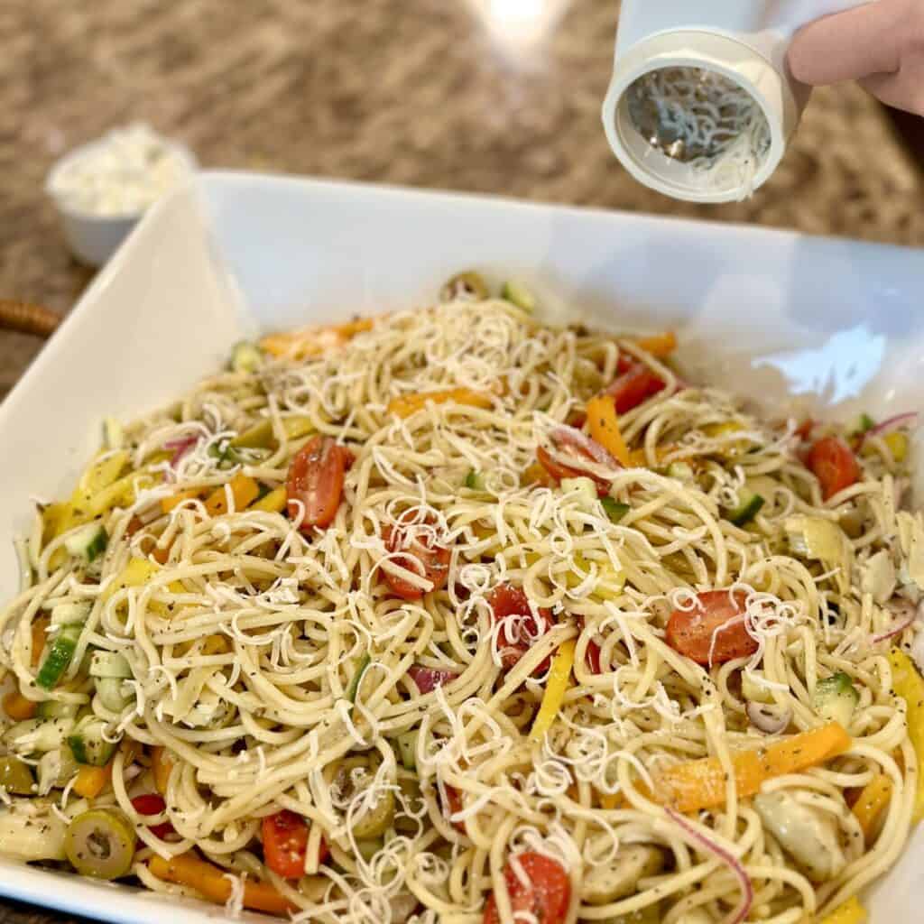 Adding parmesan to the top of cold spaghetti salad.