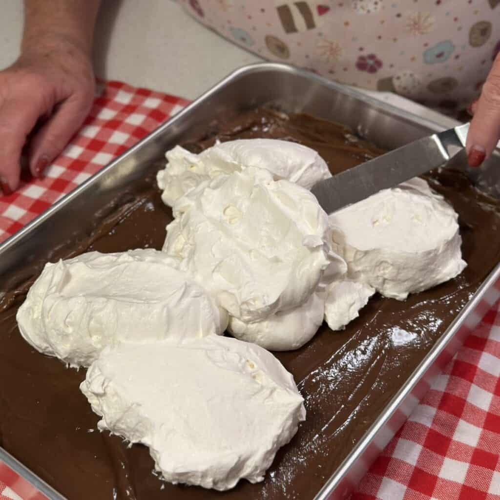 Spreading whipped cream on a chocolate layer on a dessert.