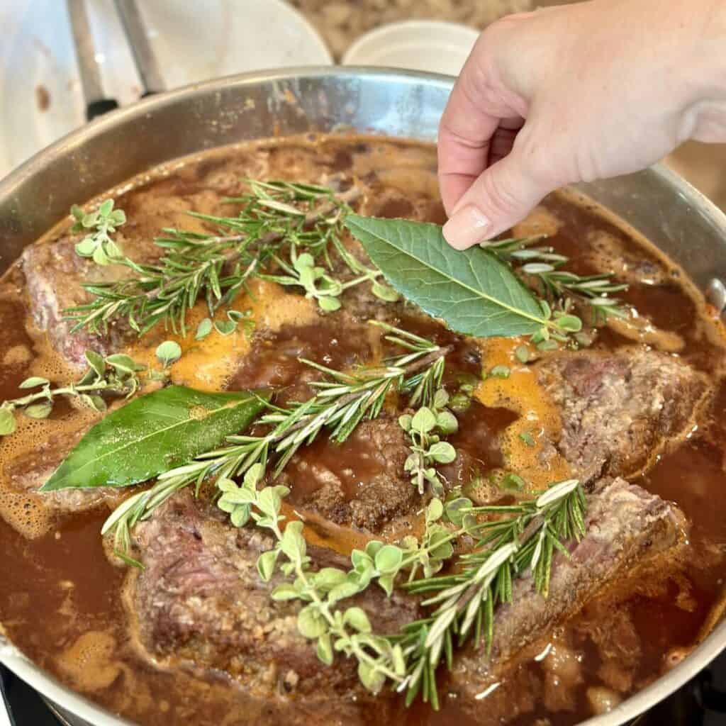 Adding fresh herbs to braised short ribs in a pan.