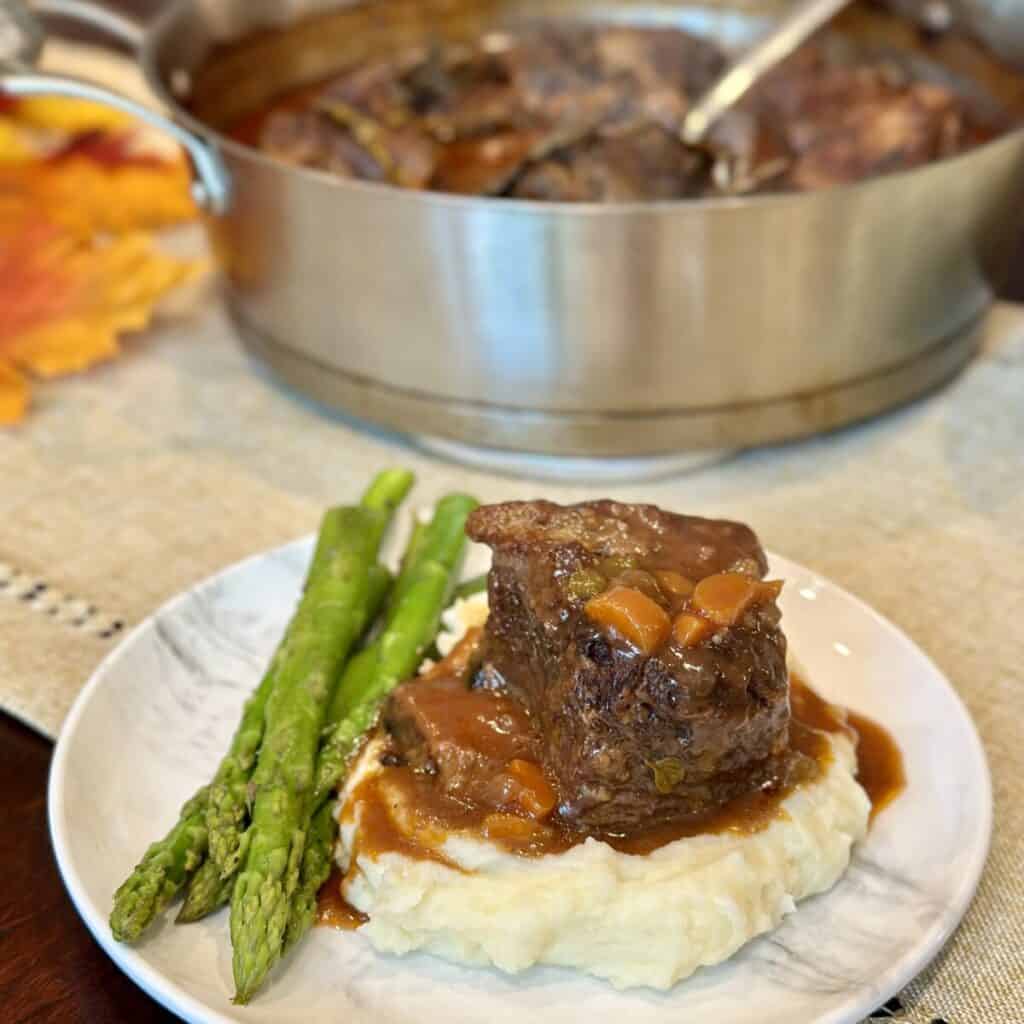 A plate with mashed potatoes, asparagus and braised short ribs.