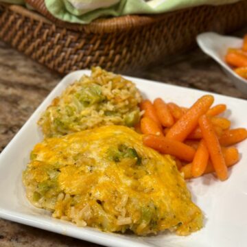 A plate of cheesy chicken broccoli and rice and carrots.