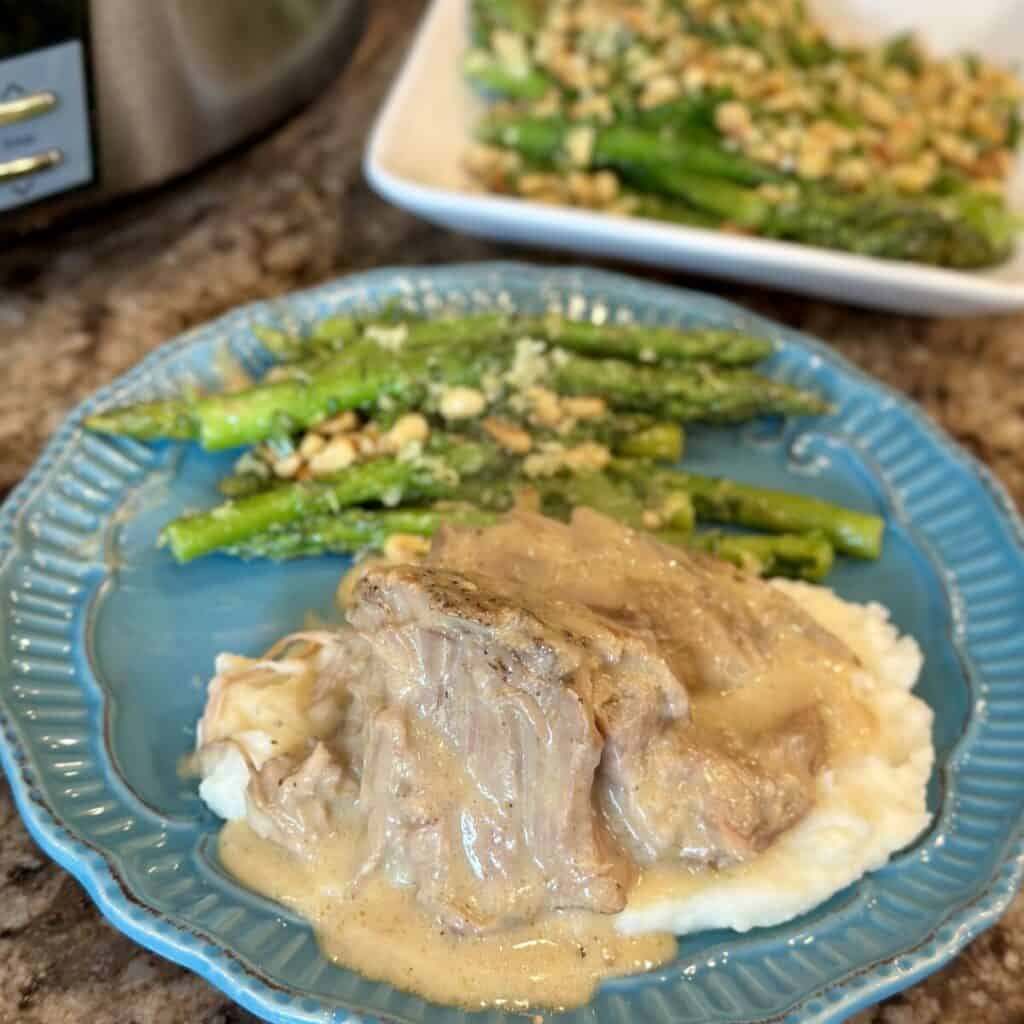 A plate of asparagus and pork roast with gravy.