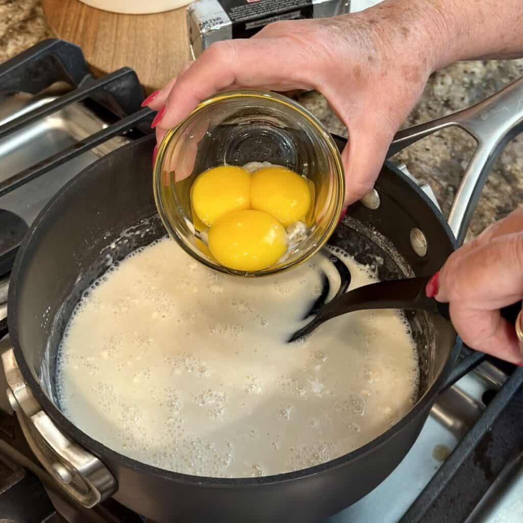 Adding egg yolks to a saucepan for pudding.