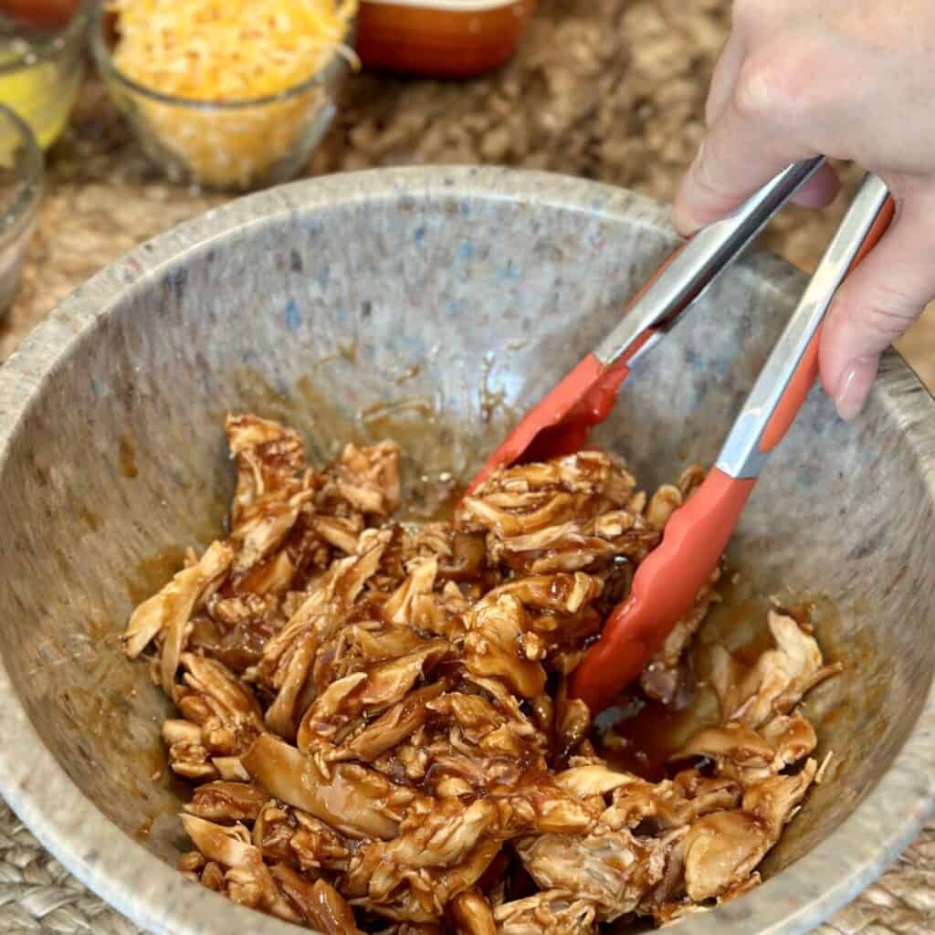 Mixing together chicken and barbecue sauce.
