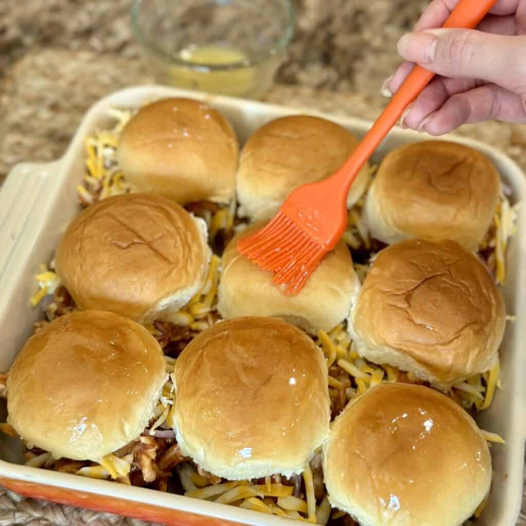 Brushing butter on top of buns in a pan.