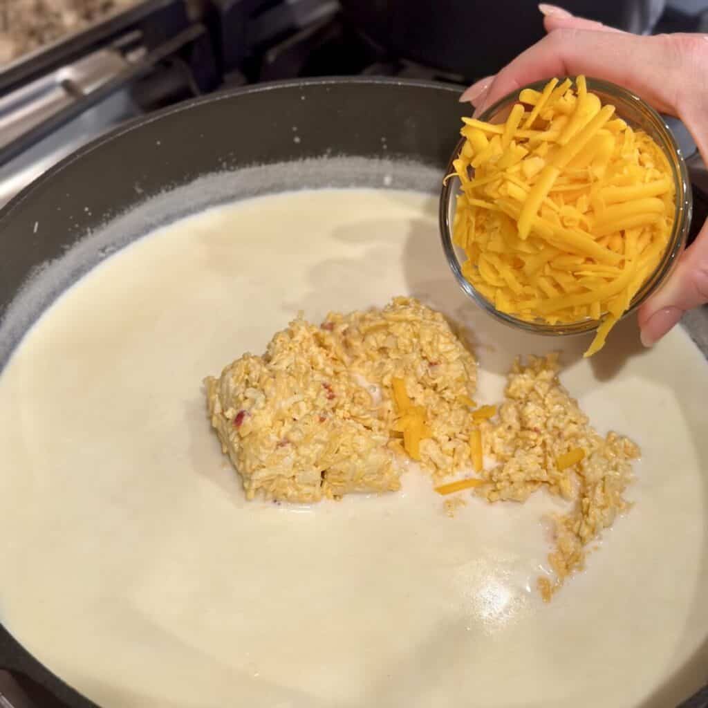 Adding pimento cheese and sharp cheddar cheese to milk in a pan.