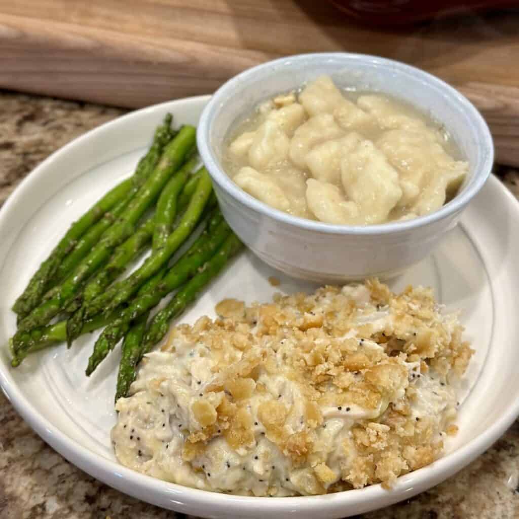A plate of chicken poppyseed casserole, dumplings, and asparagus.