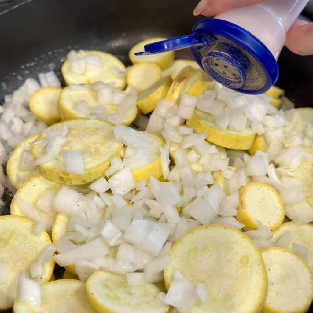 Seasoning squash and onion in a pan.