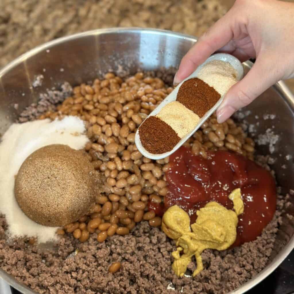 Adding seasoning to a pan of baked beans.
