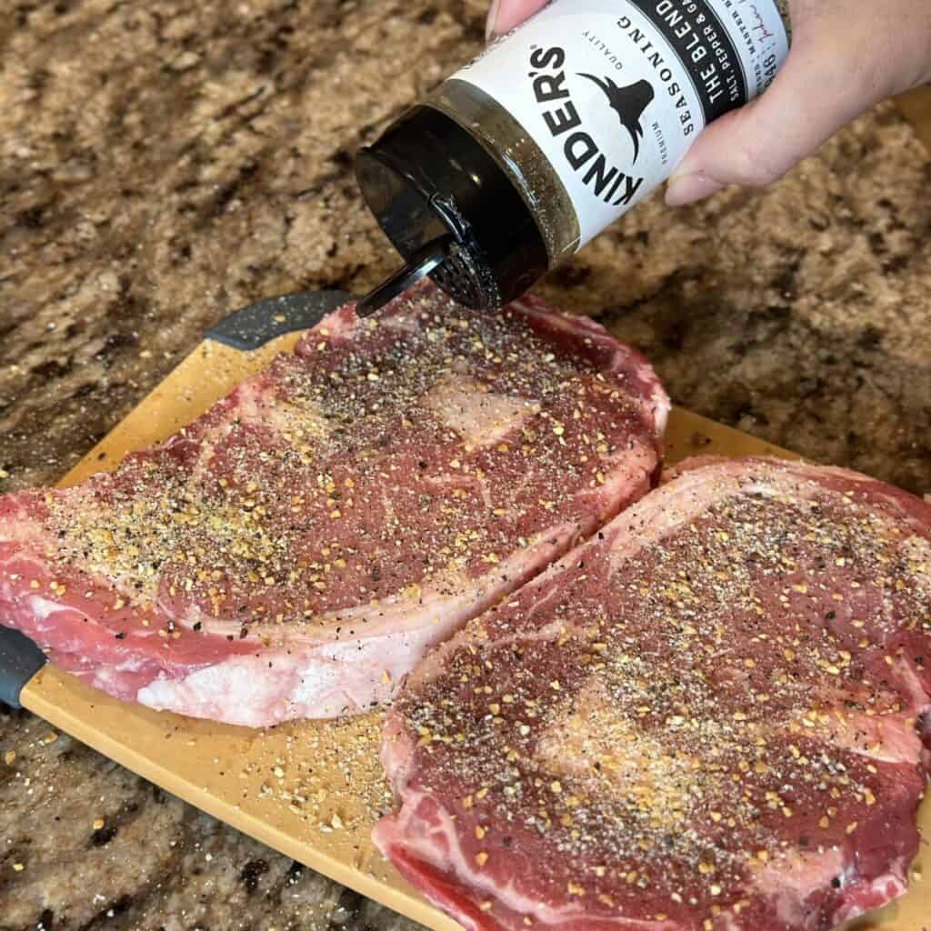 Seasoning steaks on a cutting board.