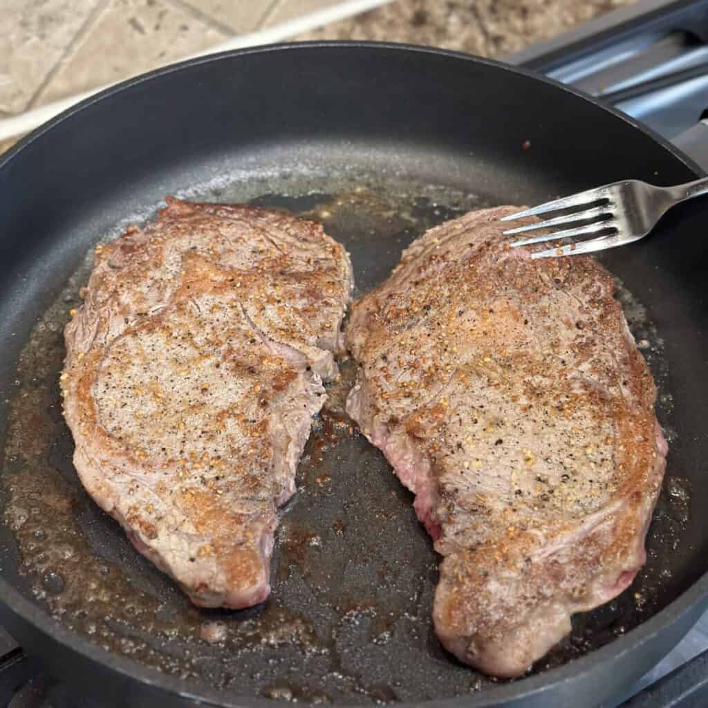 Cooking steaks in a skillet.