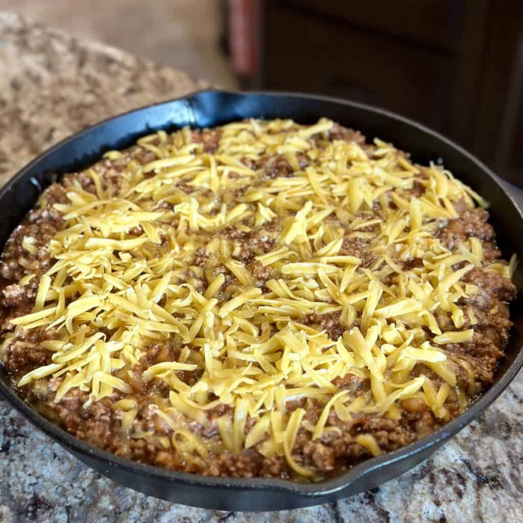 Cheese on top of sloppy Joe mix in a skillet.