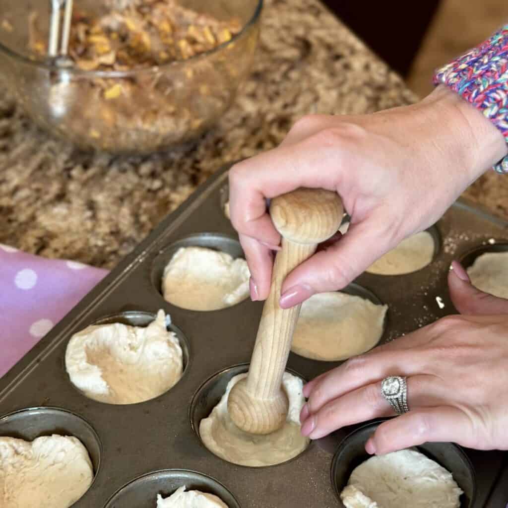 Pressing biscuit dough in a muffin pan.